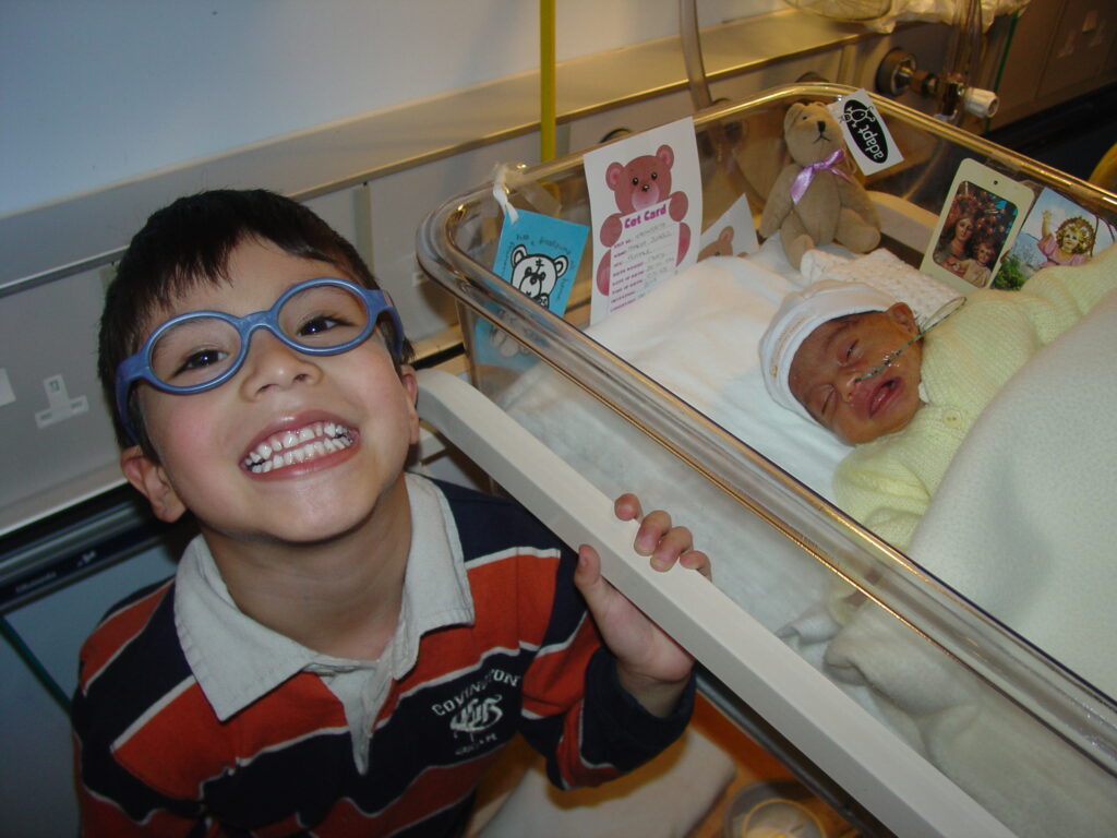 Image of Maria Paula born prematurely in 2004 lying in a cot with her brother smiling at the camera