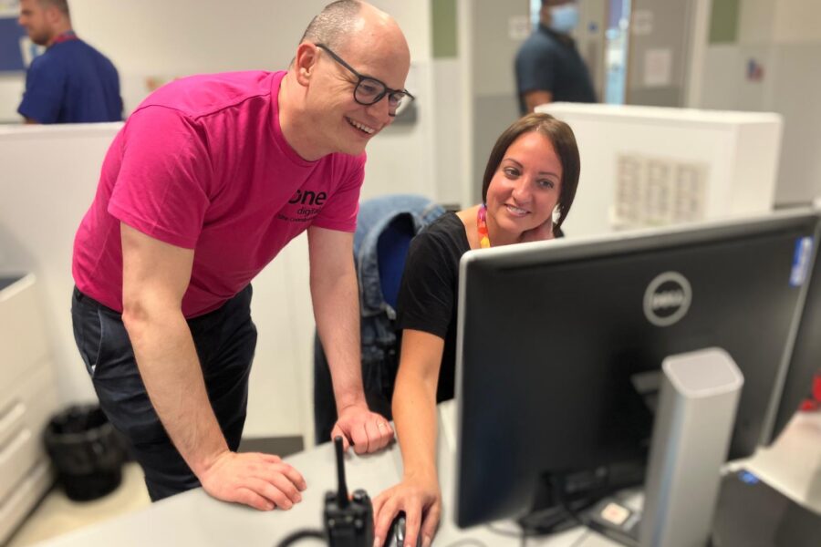 A picture of two colleagues looking at a computer monitor and smiling on the day of the new patient administration system switch over