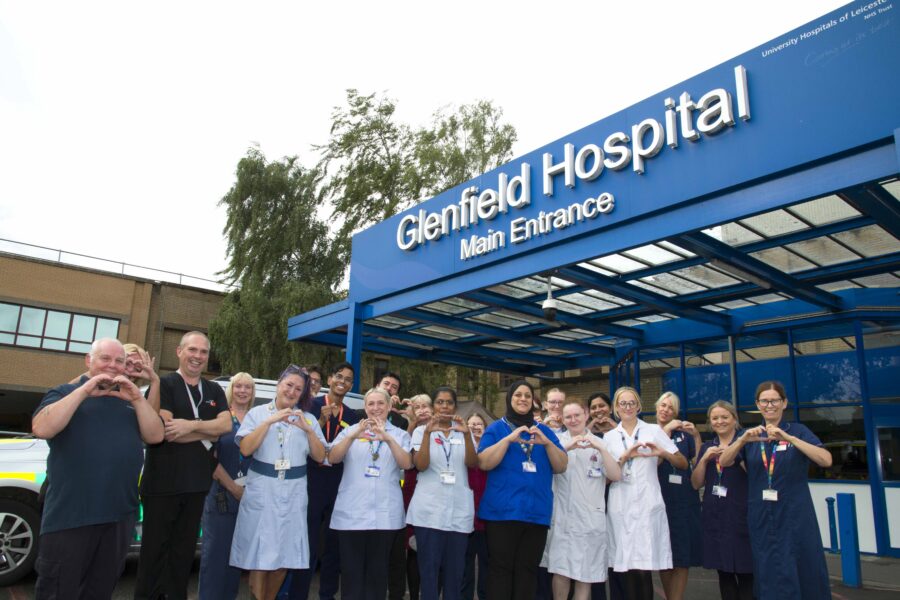 A group of colleagues stand outside the entrance to the Glenfield Hospital