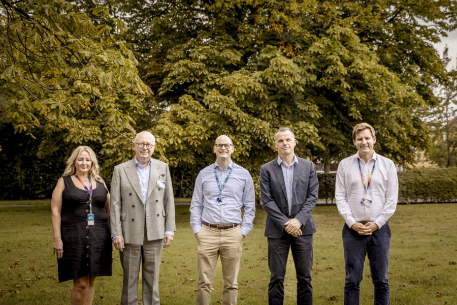 Colleagues standing smiling, with greenery in the background
