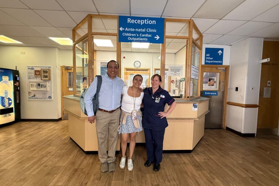A grown-up Maria Paula stands smiling between her father and the Leicester Royal Infirmary maternity matron Jenny Russell in the hospital reception