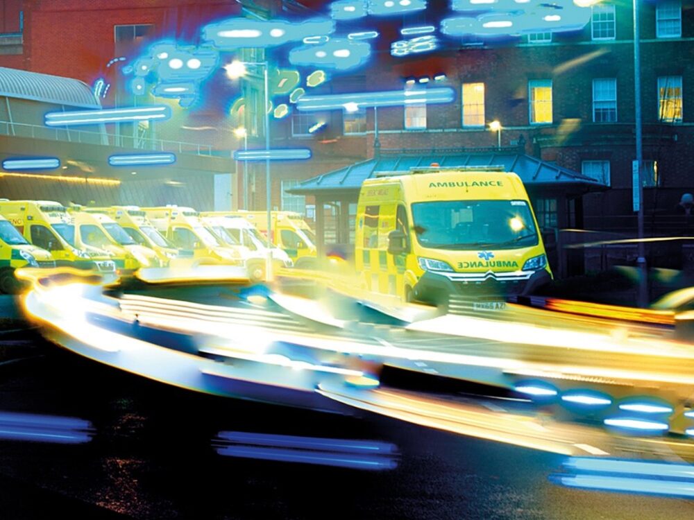 An ambulance driving at speed. There are light trails around the ambulance